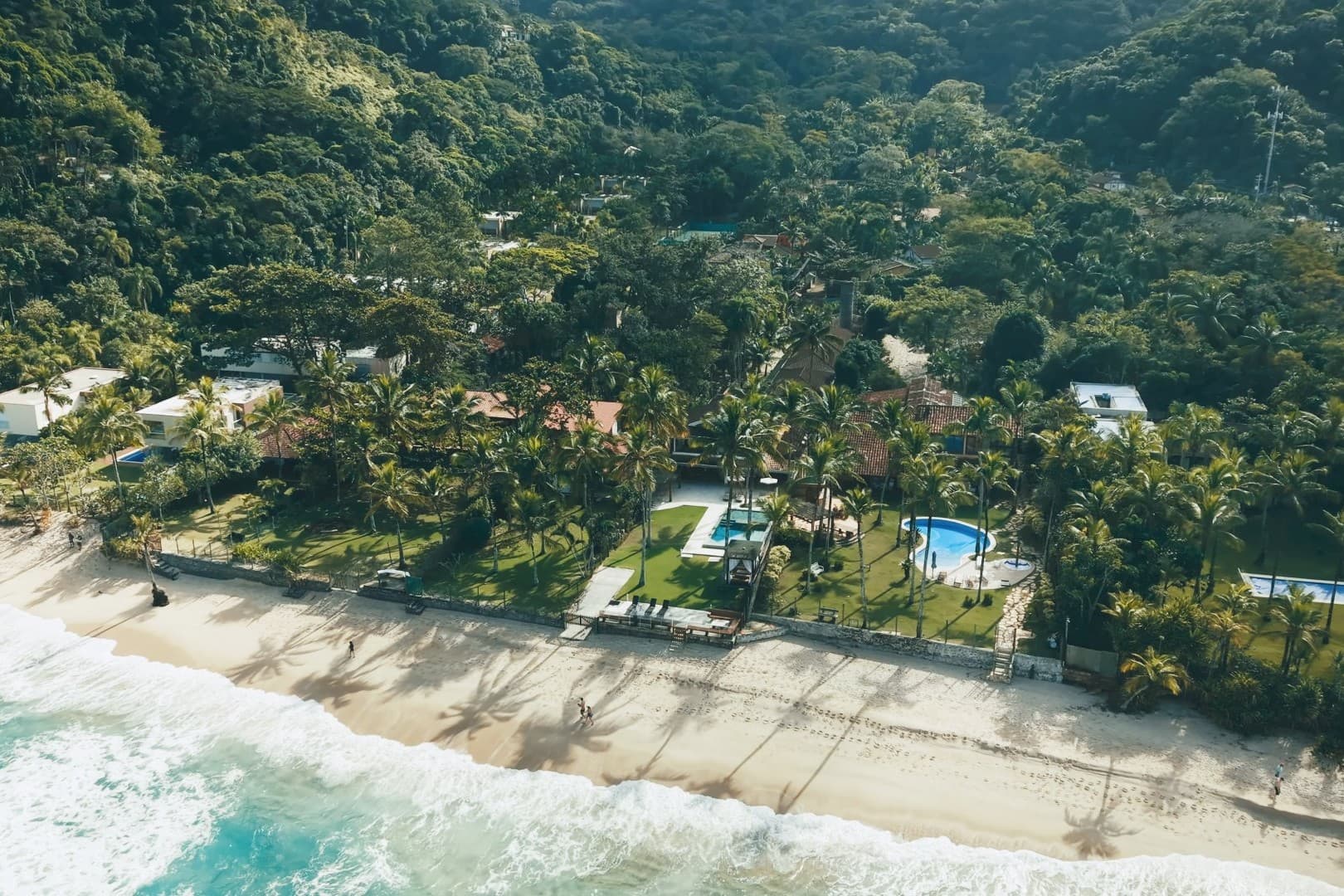 Vista aérea da orla de Maresias, com a Mata Atlântica descendo até a areia e as casas na faixa de praia